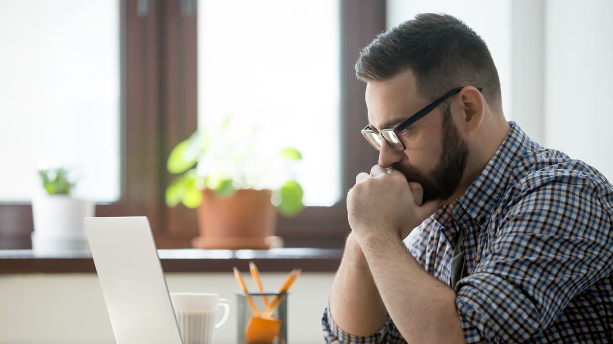 A man sitting at a desk with a laptop in front of him.