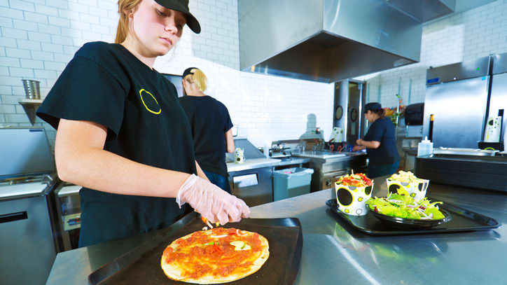A woman is preparing a pizza in a kitchen.
