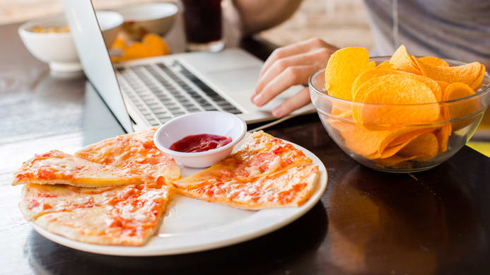 A man sitting at a table with a laptop and chips.