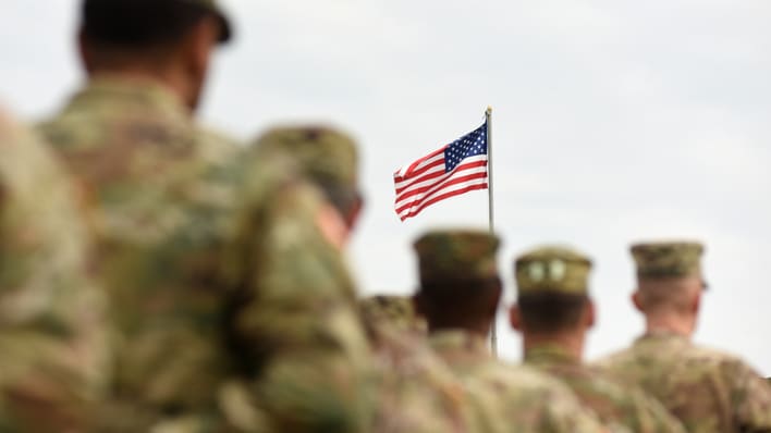 A group of soldiers are standing in front of an american flag.