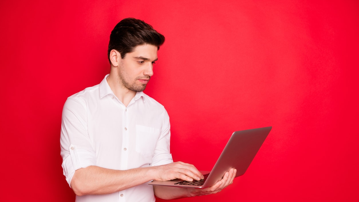 A man using a laptop on a red background.