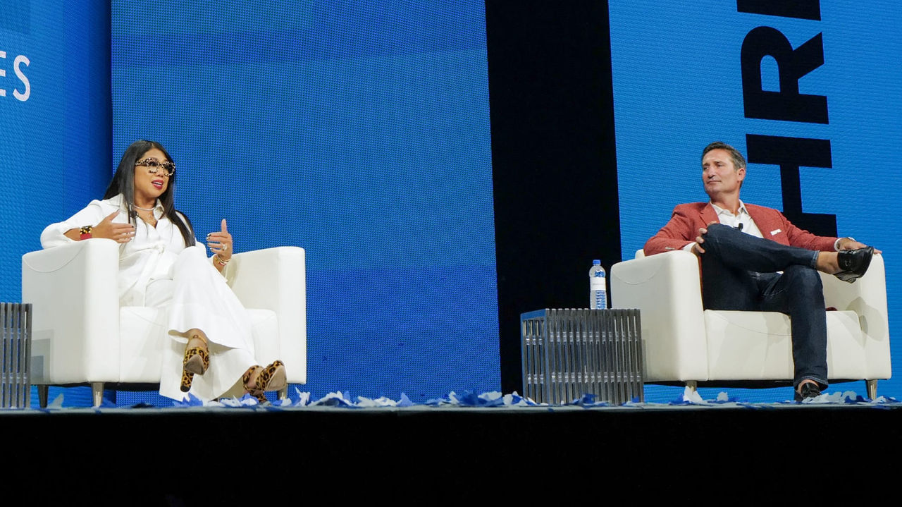 Two people sitting on chairs on stage at a conference.