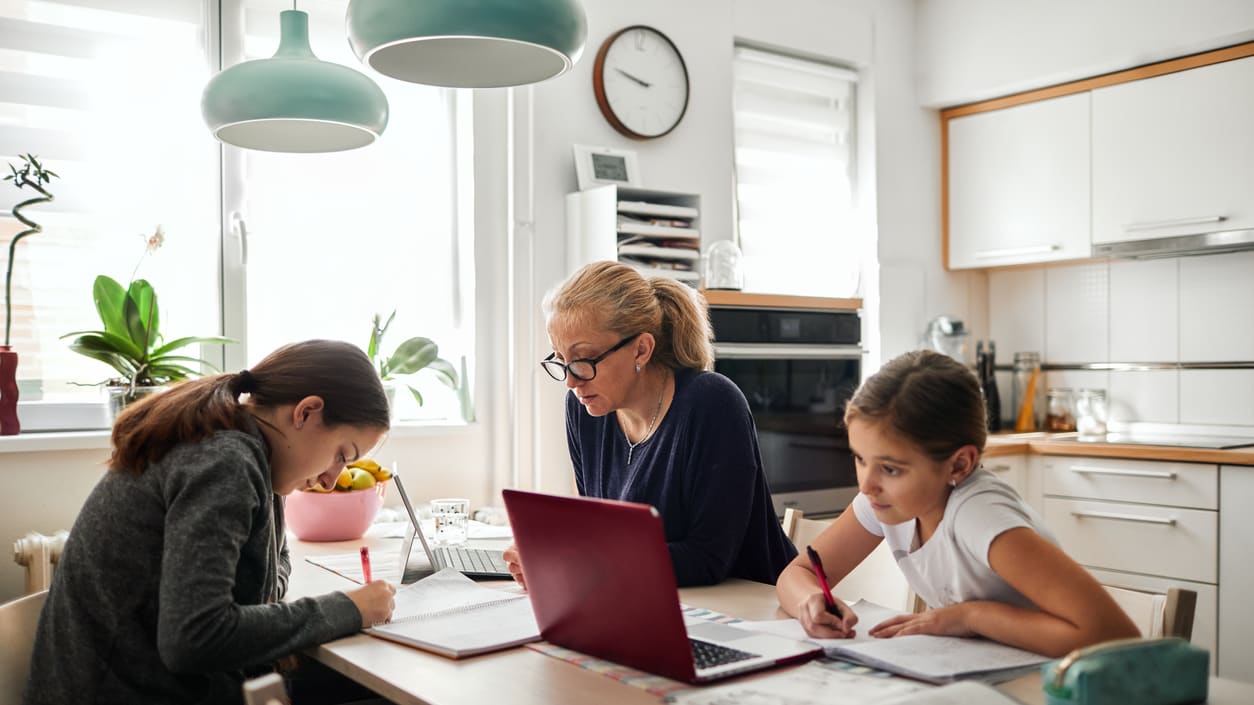 A woman and her children are working on homework in the kitchen.