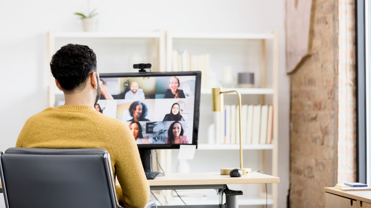 A man sitting in front of a computer with a group of people on a video call.