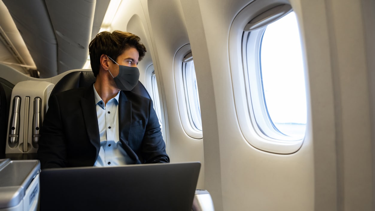 A businessman wearing a face mask on an airplane.
