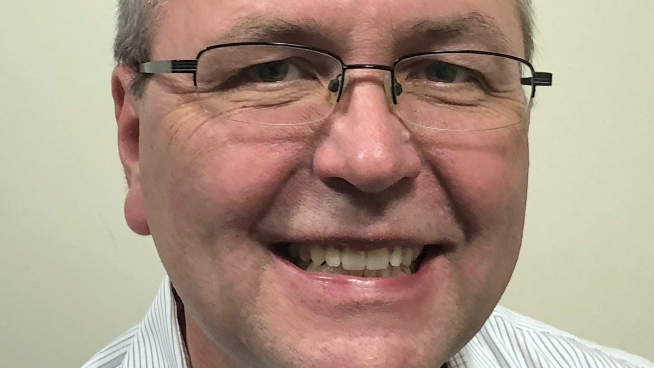 A smiling man wearing glasses and a striped shirt.