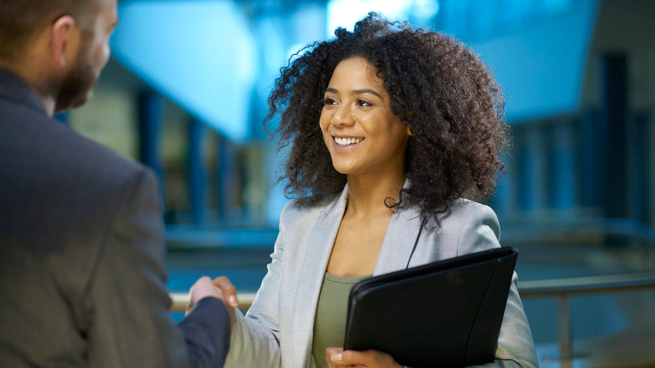 A business woman shakes hands with a man in an office.