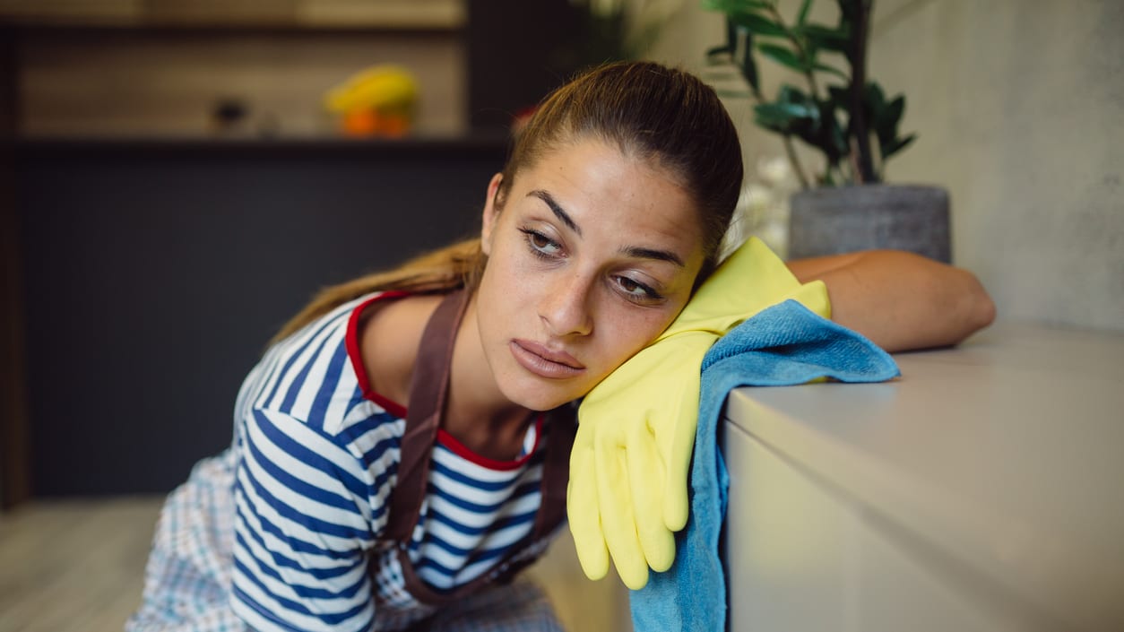 A woman in an apron leaning against a wall.