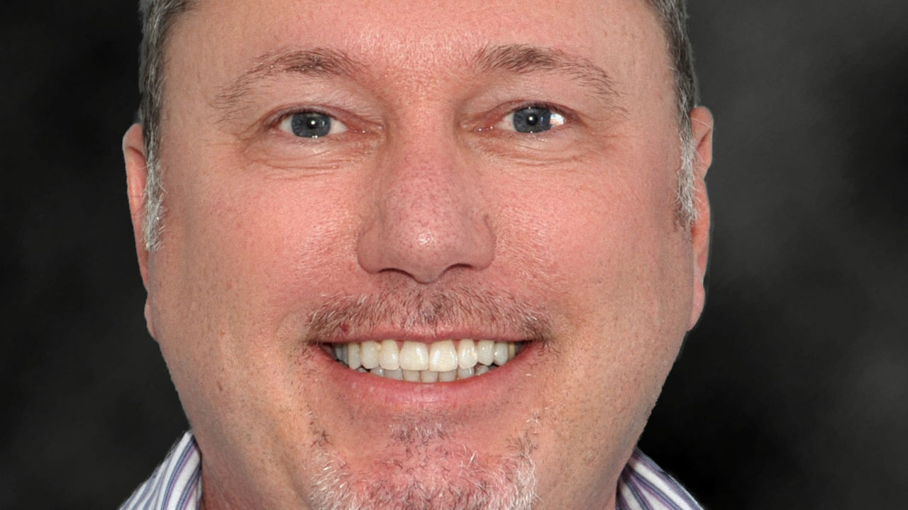 A man in a striped shirt smiling in front of a black background.