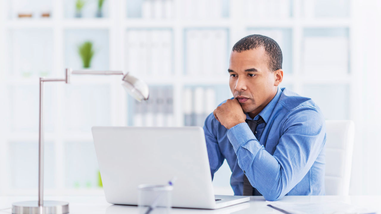 A man sitting at a desk looking at his laptop.