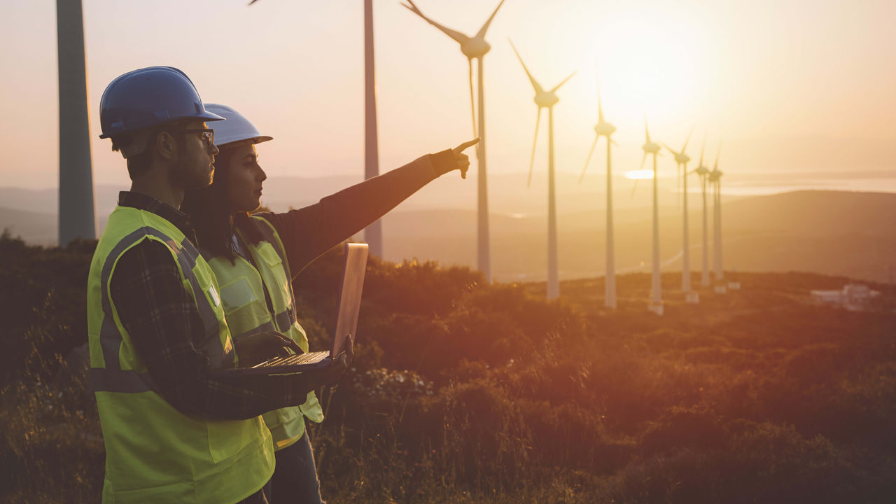 Two construction workers looking at wind turbines at sunset.