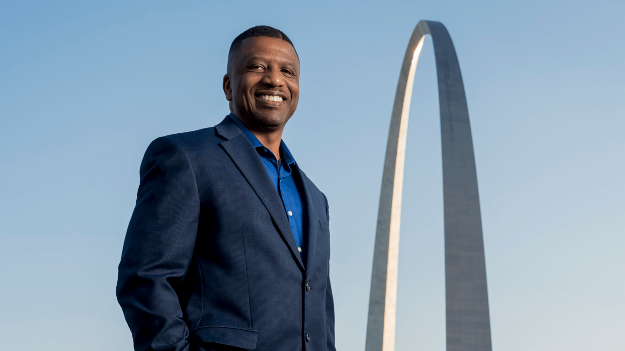 A man in a suit standing in front of the gateway arch.