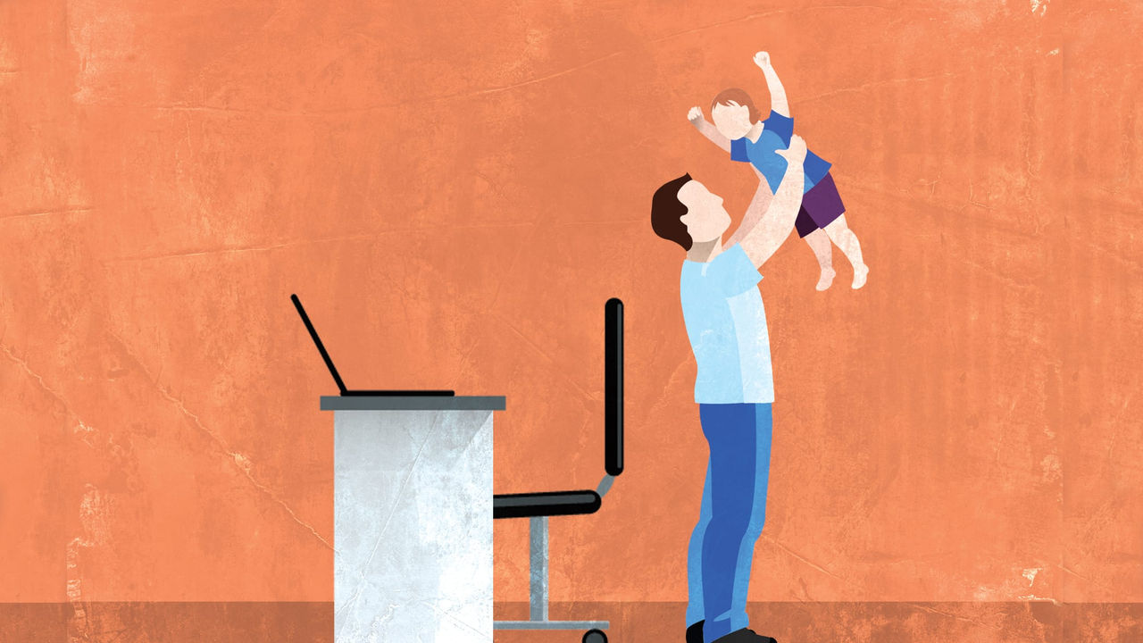 A man is holding a child while working at his desk.