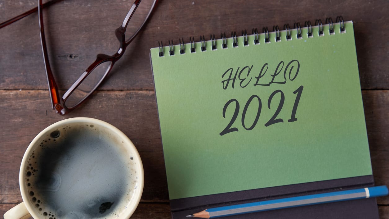 A notebook with the word hello 2021 on it and a cup of coffee next to it.