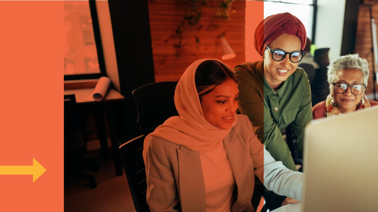 An employee and their coworkers work on a project together in front of a computer screen.