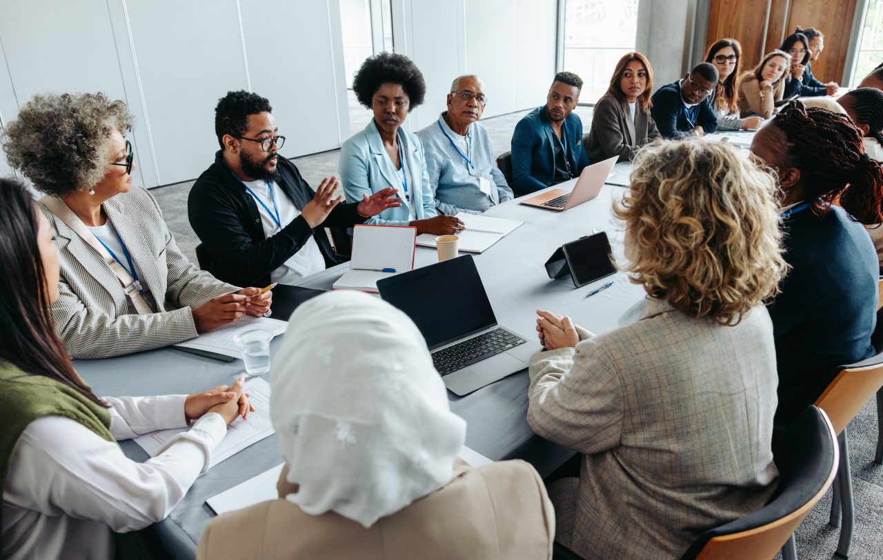 A board meeting occurs in a crowded meeting room.