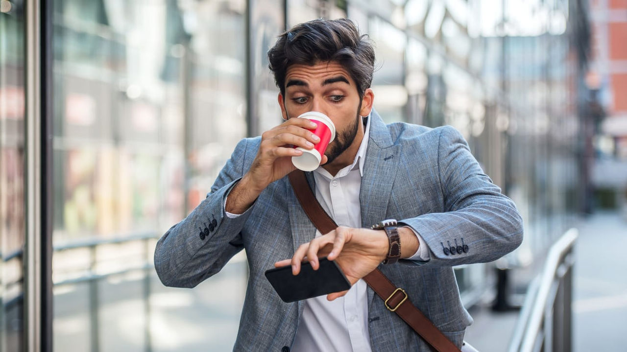 A man drinking a coffee while holding his phone.