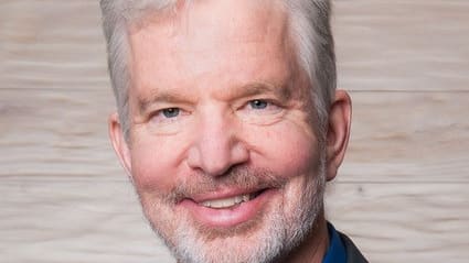 A man in a suit and blue shirt smiling.