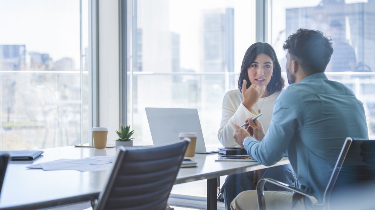 Two business people sitting at a table in an office.