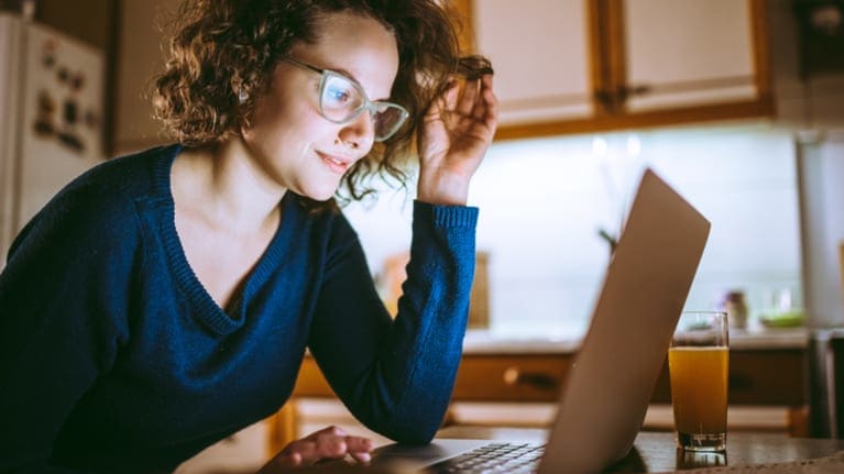 A woman is using a laptop in the kitchen.