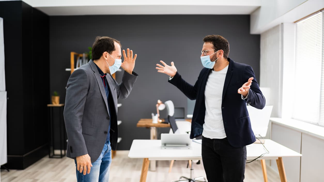 Two men in face masks arguing in an office.