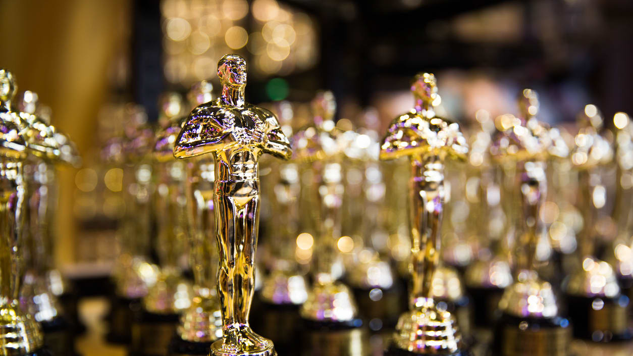 Many oscar statues are lined up on a table.
