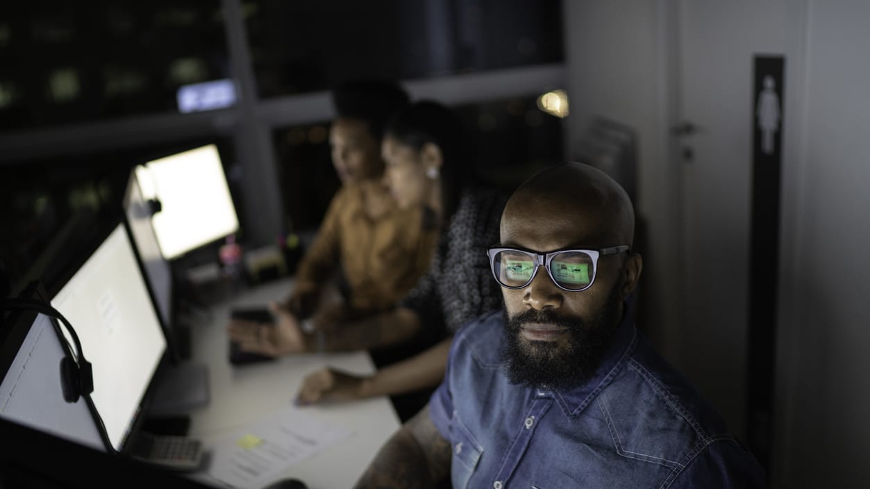 A group of people sitting in front of computers at night.