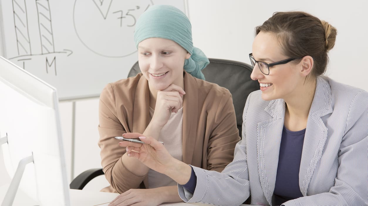 Two women sitting at a desk looking at a computer.