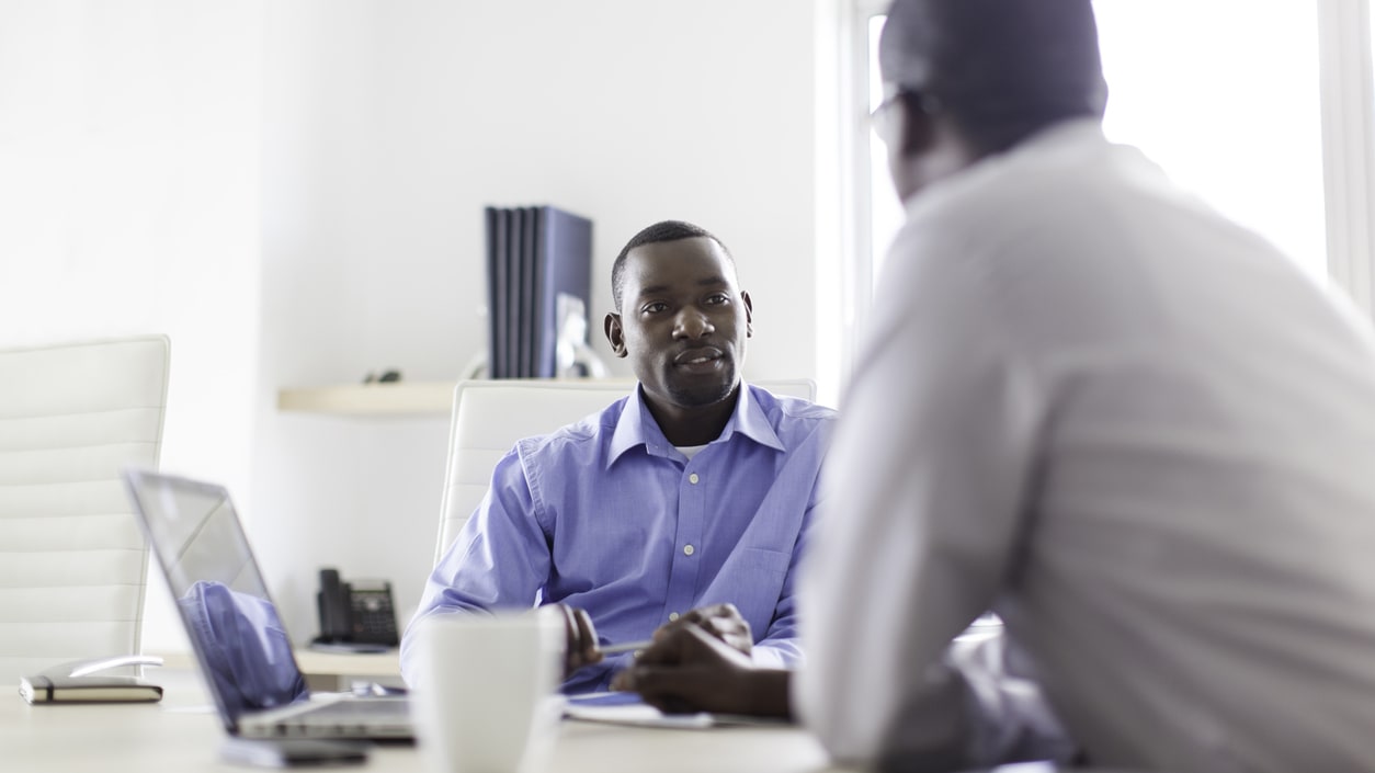 Two business men talking at a table in an office.