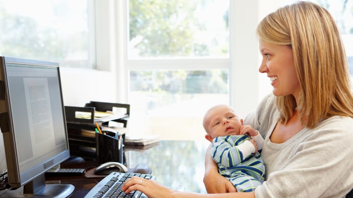 A woman holding a baby while working at her computer.