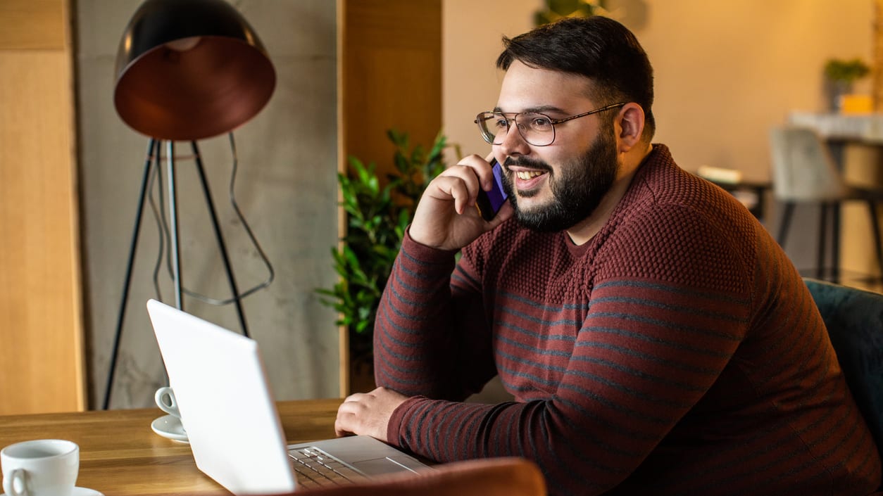 A man talking on the phone while sitting at a table in a coffee shop.