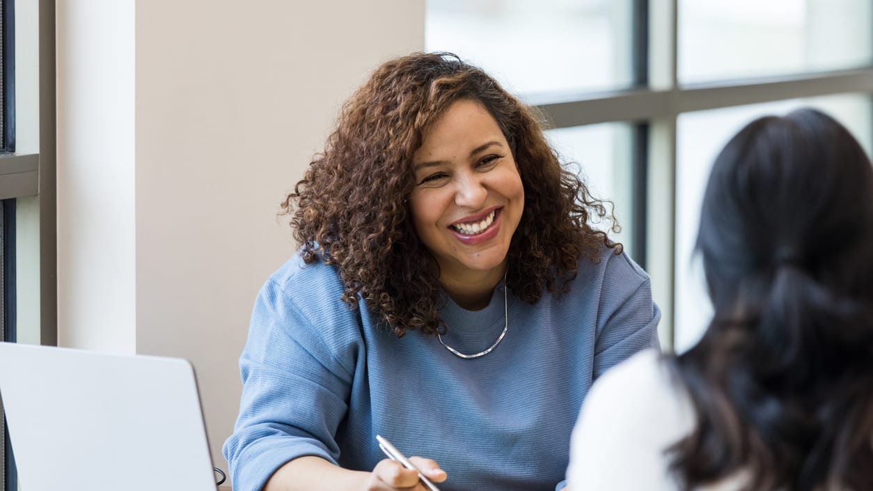 Two women sitting at a table talking to each other.