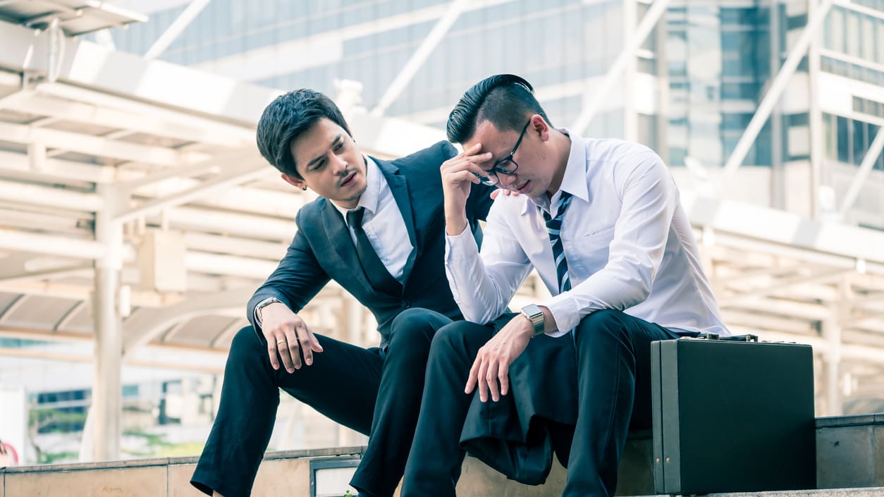 Two businessmen sitting on steps in front of a building.