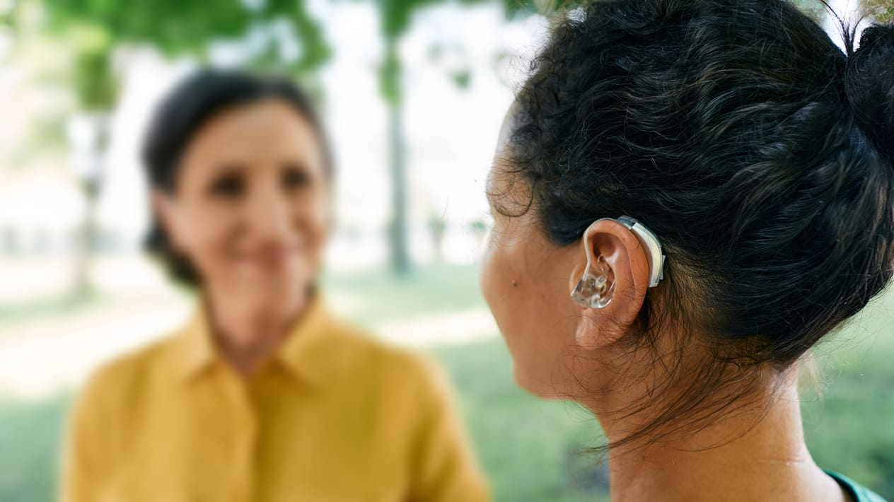 A woman with a hearing aid is talking to another woman.