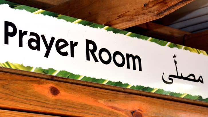 A sign that says prayer room hanging on a wooden wall.