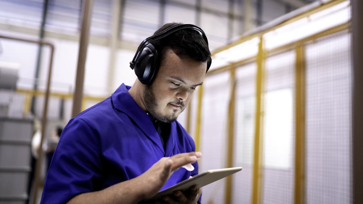 A man wearing headphones is using a tablet in a factory.