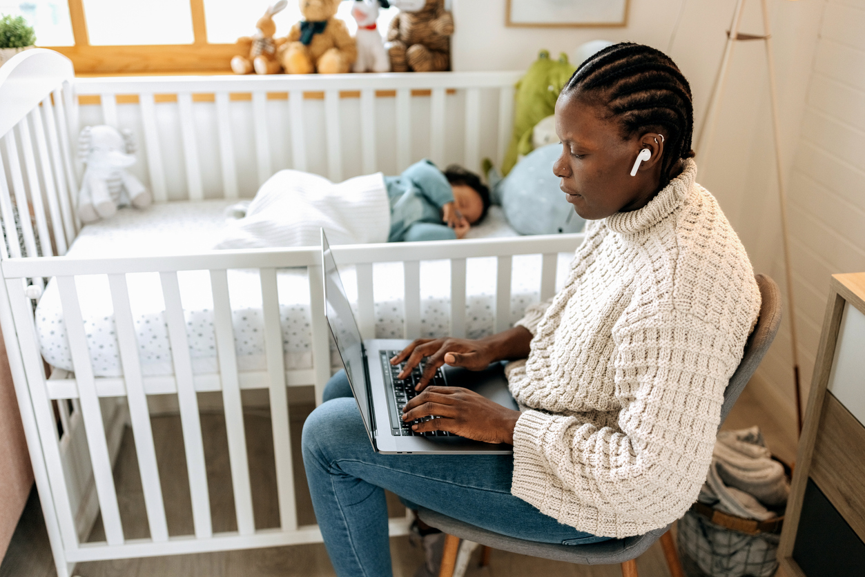 mother works on computer while baby in crib