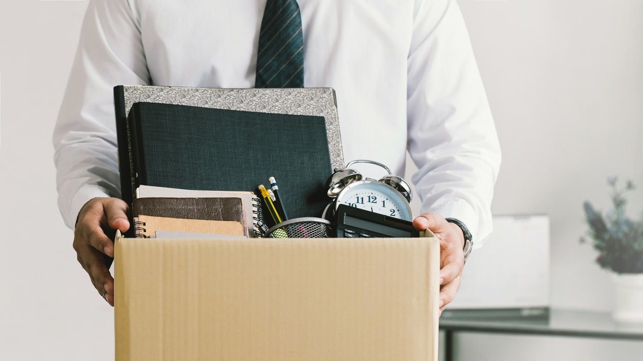 A man is holding a cardboard box full of items.