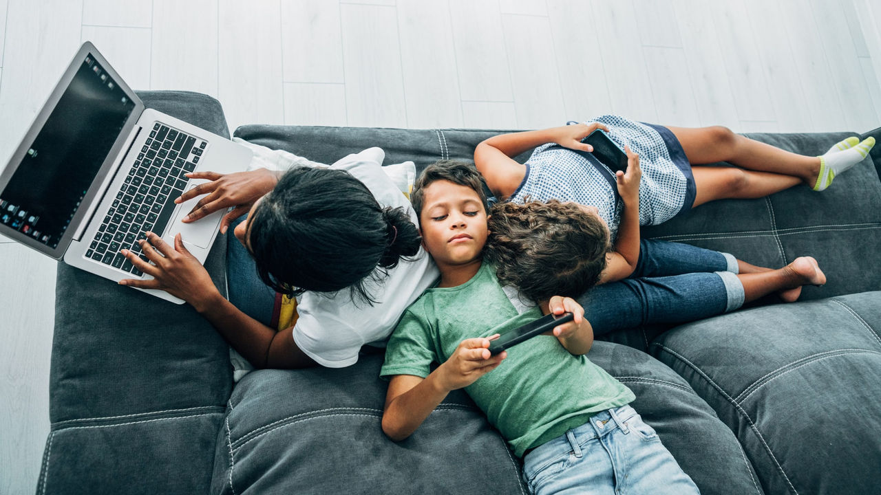 Three children laying on a couch with a laptop.