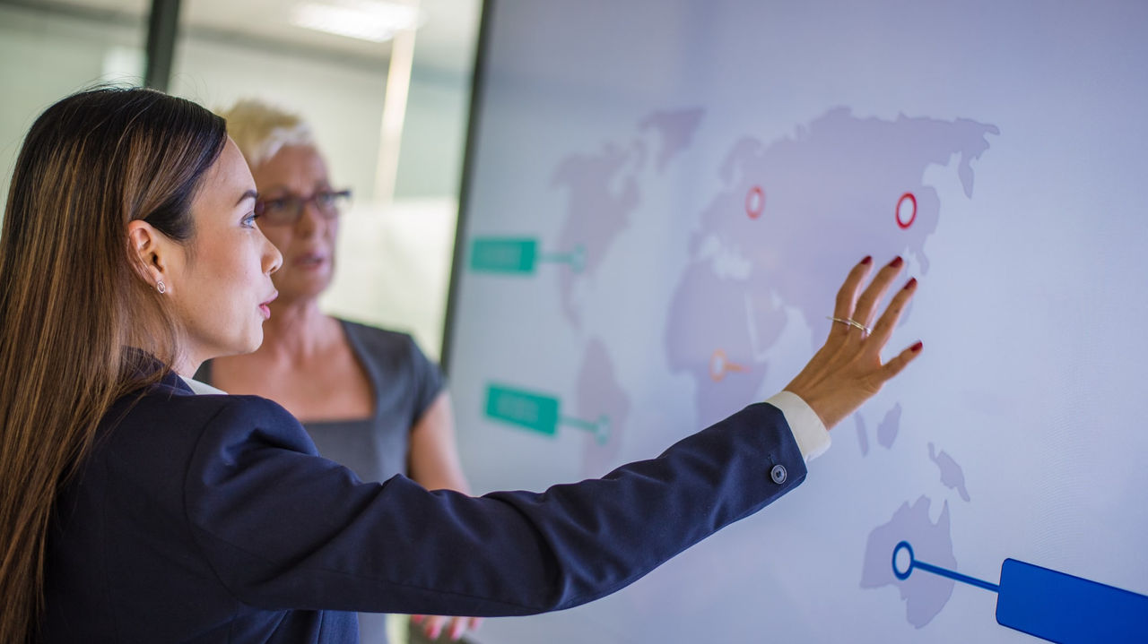 Two business women pointing at a map on a screen.