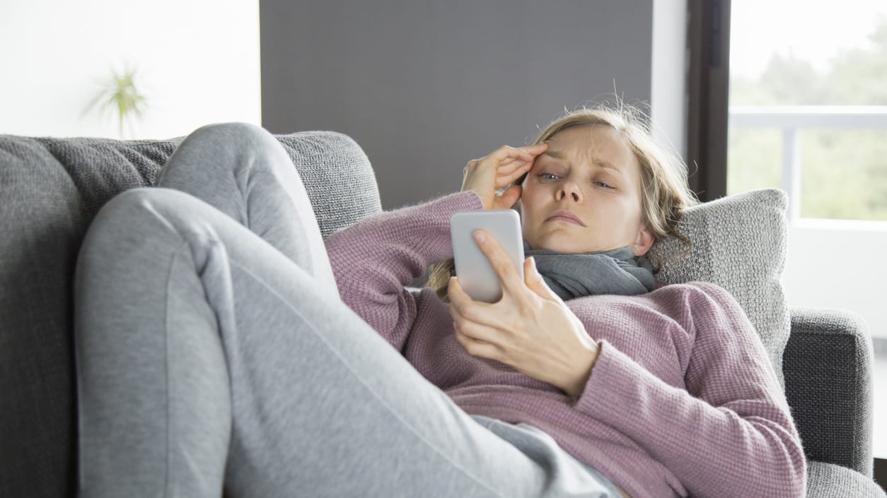 A woman is sitting on a couch with a cell phone in her hand.