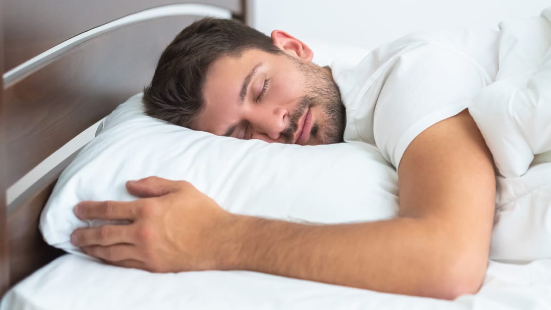 A man sleeping in a bed with a white duvet.