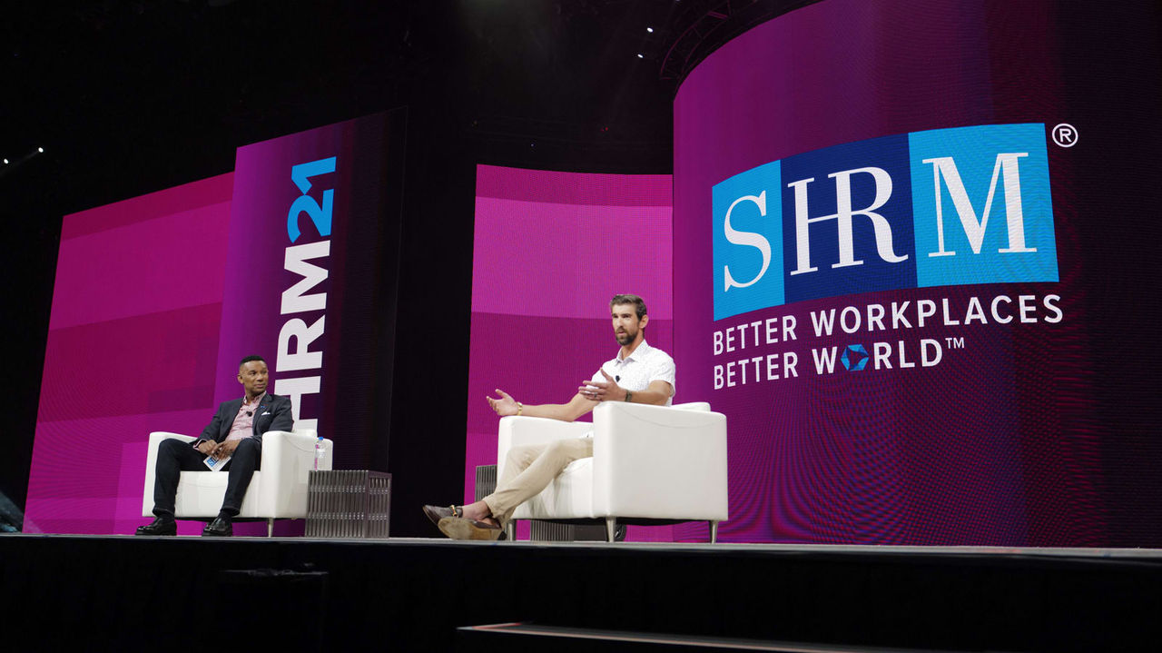 Johnny C. Taylor Jr. and Michael Phelps sitting in chairs on stage at the SHRM conference.