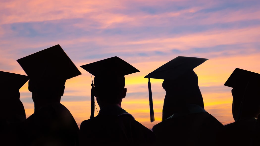 Silhouettes of graduation hats against a sunset.
