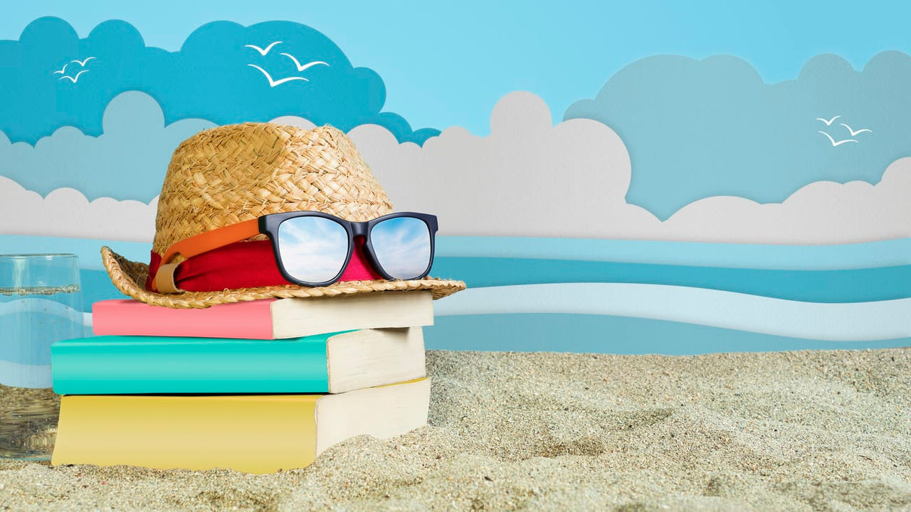 A straw hat, glasses and books on the sand.