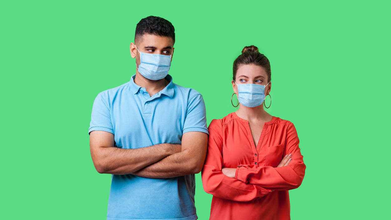 A man and woman wearing surgical masks on a green background.