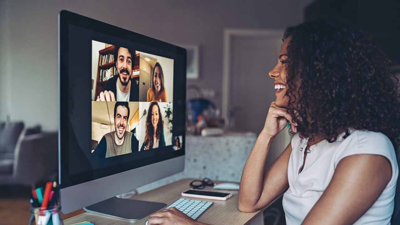 A woman is sitting in front of a computer with a group of people on a video call.