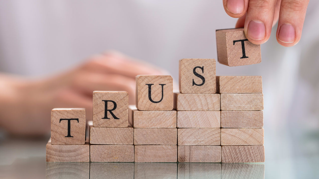 A person is putting wooden blocks with the word trust on them.