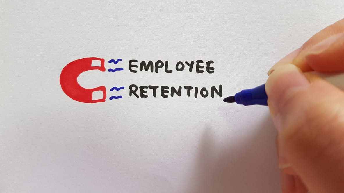A person writing the word employee retention on a piece of paper.
