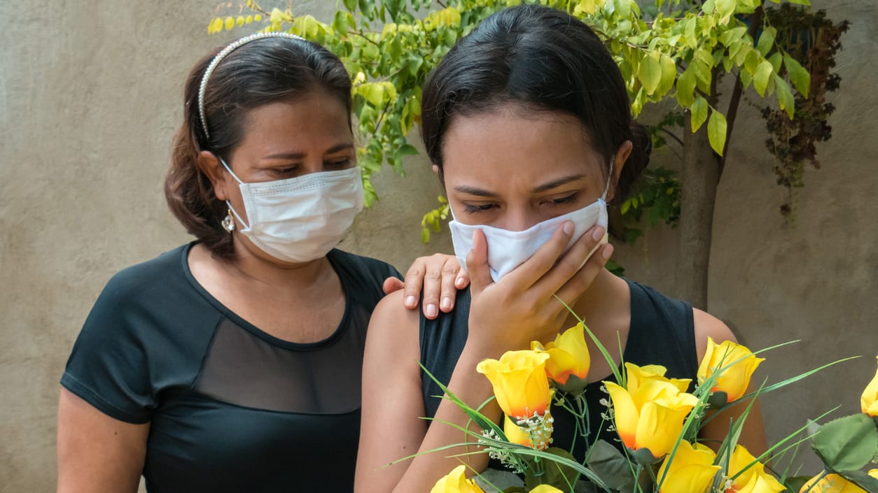 A woman wearing a face mask holds a bouquet of yellow flowers.